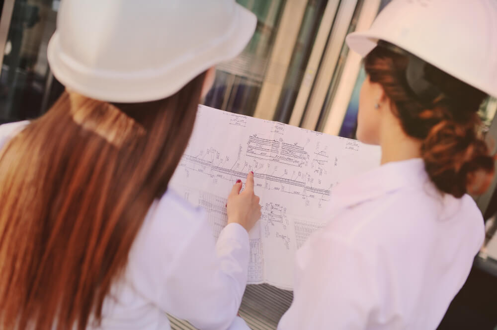 two-young-cute-girls-business-clothes-white-construction-helmets-discuss-business-plan-contract